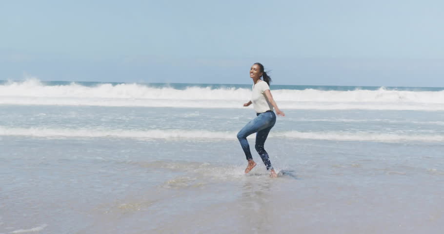 Woman lifting foot as wave touching toes, spinning on beach for health ad with light-leaks floating. Fitness, movement, outdoor, energetic, leisure, scenic, vibrant