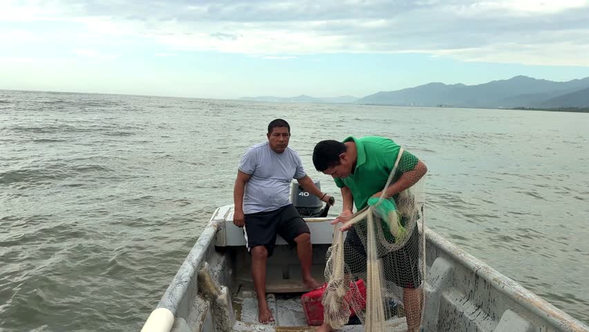Fishermen work together, casting and retrieving a fishing net from their boat on a calm sea