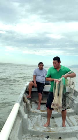 Fishermen casting fishing net from small boat in ocean