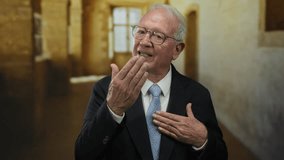 Senior man in a suit stands in an old university, hands on heart, exuding wisdom and emotion in an academic setting, creating a blend of business and heritage. - Powered by Shutterstock - Get 15% off with code: PIKWIZARD15