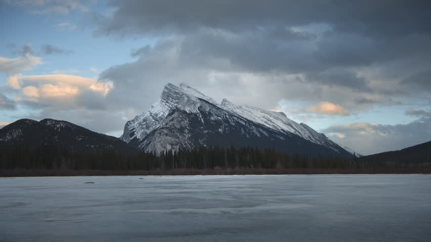 Clouds moving above frozen lake at sunset. Mount Rundle, Banff. Time Lapse.