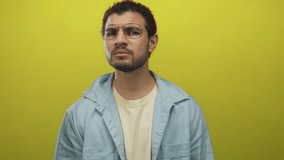 Man beckons hand in yellow studio with serious gaze and visible gesture near face wearing casual shirt; curiosity. - Powered by Shutterstock - Get 15% off with code: PIKWIZARD15