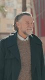 Vertical video, Portrait of a happy senior man with grey hair and beard smiling and looking around a city street on a sunny day. - Powered by Shutterstock - Get 15% off with code: PIKWIZARD15