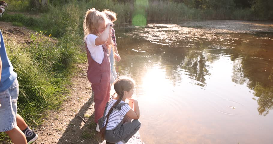 Children spending time by lake in nature. Camera moving right