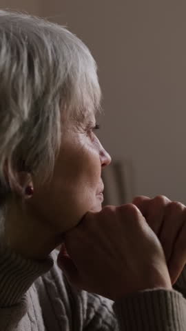 Vertical video, An elderly woman with gray hair sits alone at her table, lost in thought, possibly dealing with loneliness or depression.