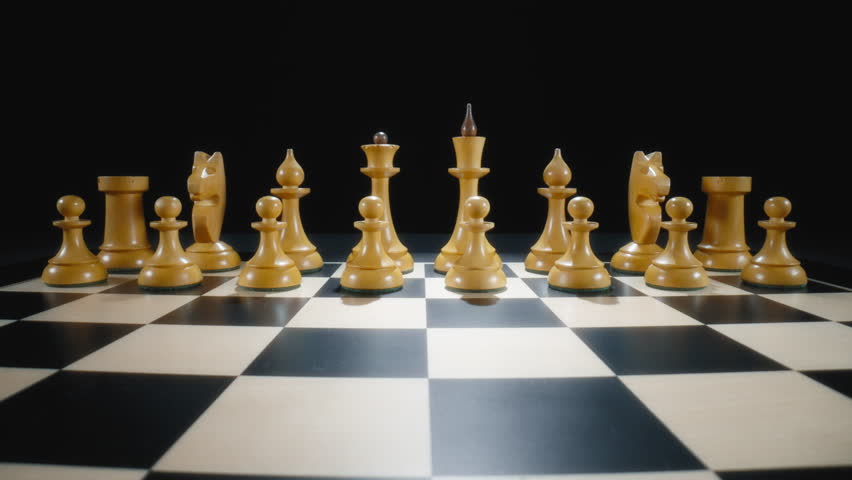 Dolly out macro shot of wooden chess pieces on a chessboard. Slow motion.