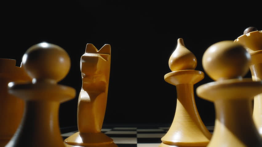 Dolly macro shot of white wooden chess pieces on a chessboard. Slow motion.