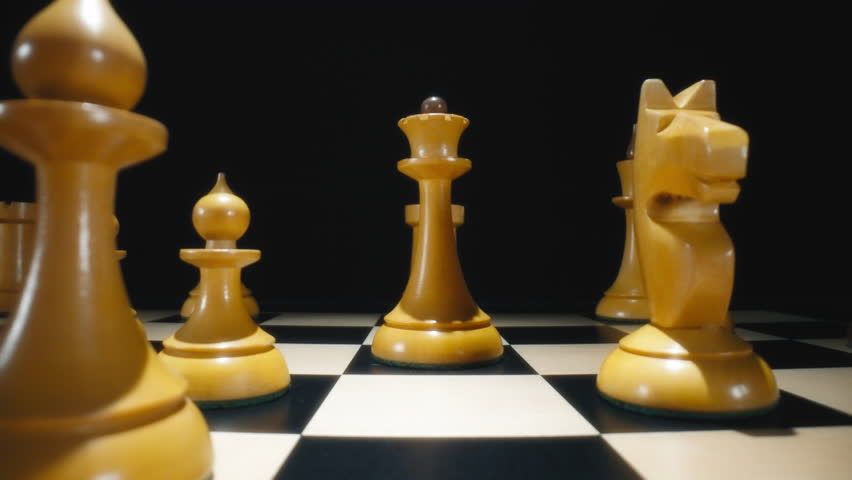 Player hand moving white queen chess piece on a chessboard. Dolly macro shot, slow motion.