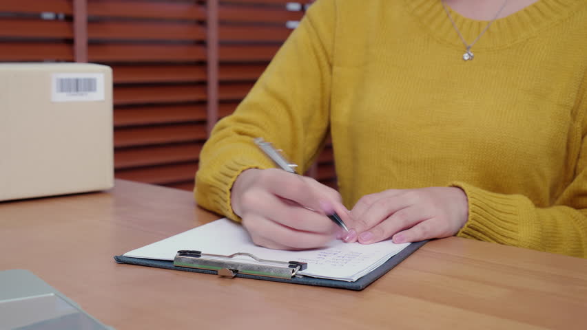 Small business writing customer order on clipboard for preparing package for shipping in home office, e‑commerce startup, online shop, entrepreneur check shipping with writing on document.