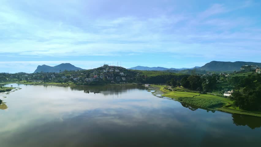 Beautiful aerial drone footage flying from the still waters of Lake Gregory toward the elevated urban sprawl of Nuwara Eliya, Sri Lanka. Perfect for tourism, landscape, or city promo.