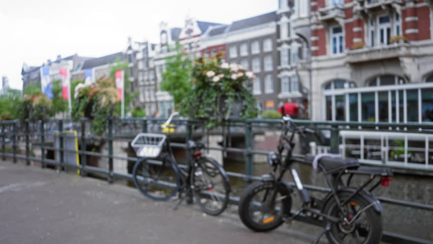 Bicycles parked on a bridge in amsterdam with blurred canals and historic buildings in the background, capturing the vibrant urban ambiance of the netherlands.