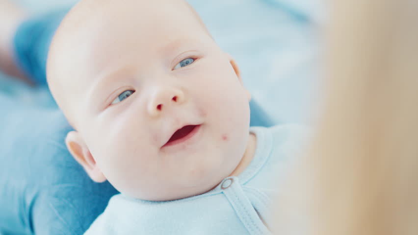 Mother plays with her newborn son with deep blue eyes in a bright room