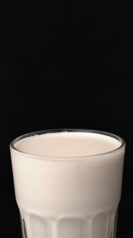 Hand dips chocolate chip cookie into white milk glass on black background with soft lighting, for snack product scene.