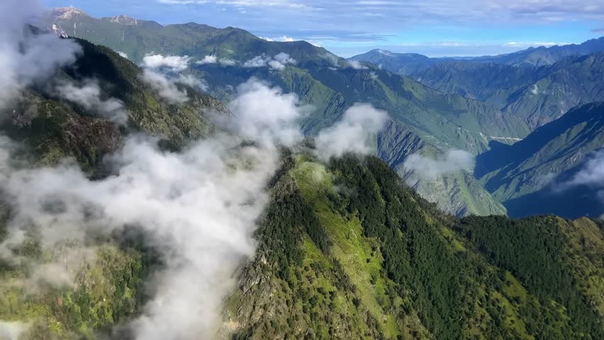 A drone soars smoothly over mist-covered mountains, revealing dramatic peaks and atmospheric fog in a serene, high-altitude landscape.