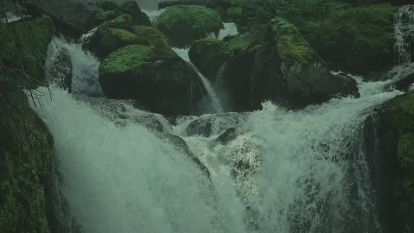 Multiple mountain streams flow from various points, crashing against rocks and converging into a single powerful torrent rushing downwards.