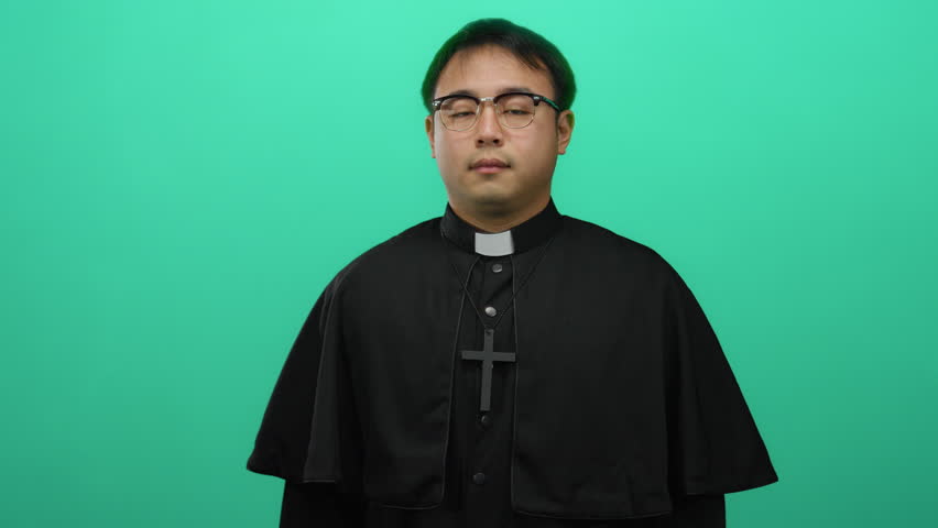 Asian priest gesturing silence against a bright green background, wearing glasses and a clerical collar, suggesting a concept of confidentiality or introspection.