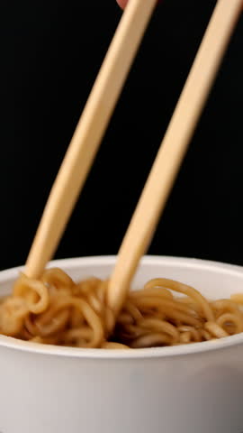 Chopsticks lift glossy noodles from warm soup cup with soft steam reflections, for instant food packaging mockup.