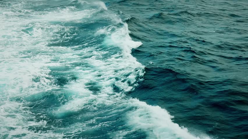 A vibrant and intense view of a stormy ocean surface filled with large, crashing waves. White foamy crests break dramatically, contrasting with deep blue and greenish waters beneath.