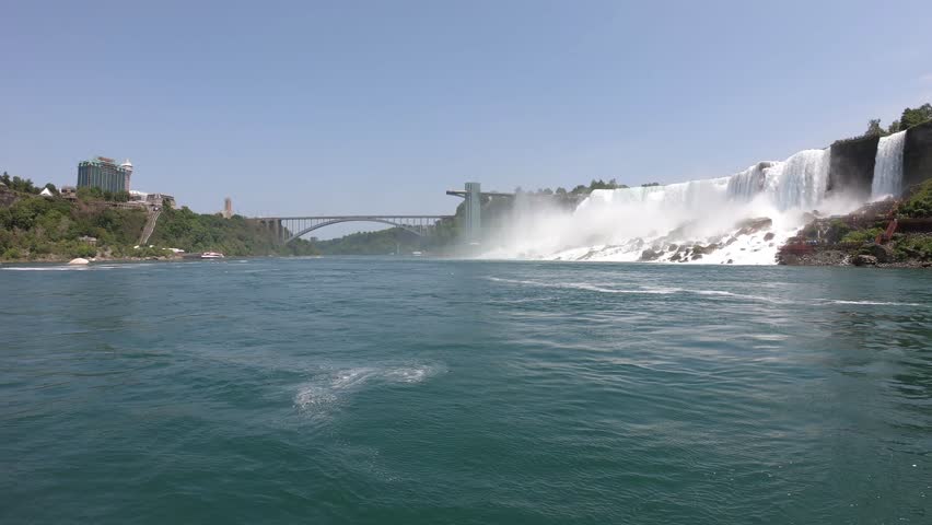 DOLLY SLOW MOTION - The Niagara Falls (American Falls and Bridal Veil Falls), Rainbow Bridge, and the Prospect Point Observation Tower seen from a boat tour on the Niagara River in Ontario, Canada.