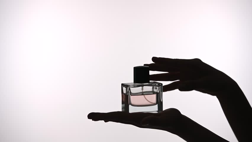A silhouetted view of a perfume bottle is delicately held in hands, showcasing elegance and simplicity.