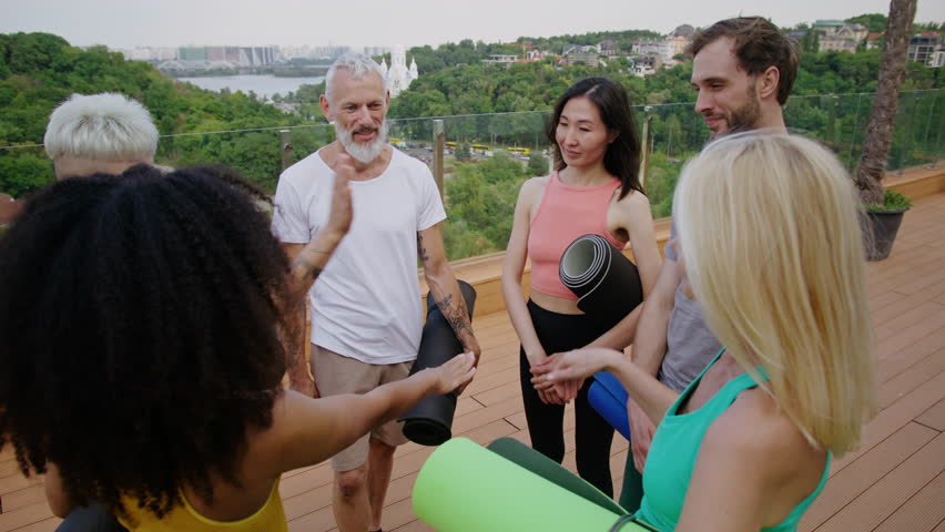 Multigenerational sportsmen join hands in symbolic gesture expressing happiness on hotel rooftop. Mixed race friends share good mood at yoga lesson in city park