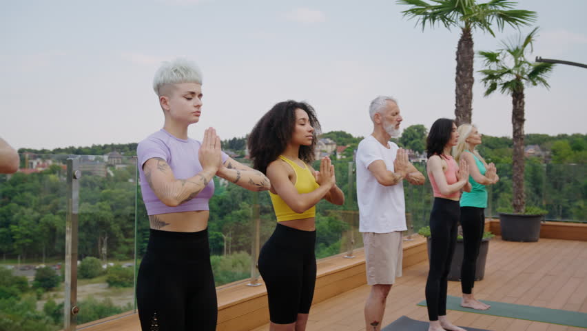 Concentrated multiethnic sportspeople meditate standing on hotel roof terrace. Multigenerational yoga practitioners hold hands in namaste sign at resort - Powered by Shutterstock - Get 15% off with code: PIKWIZARD15