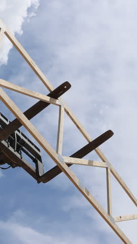 Construction workers operate telehandler crane to raise large wooden beams at building site under frame assembly