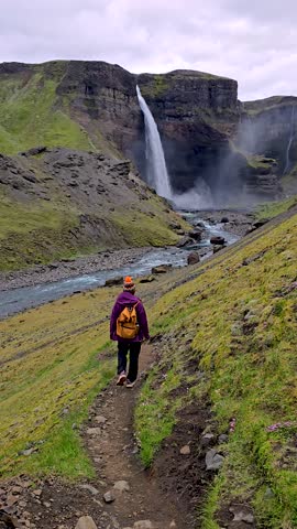 A hiker explores the lush landscape leading to Haifoss, one of Icelands most breathtaking waterfalls. The serene atmosphere and cascading water offer a perfect escape into nature.