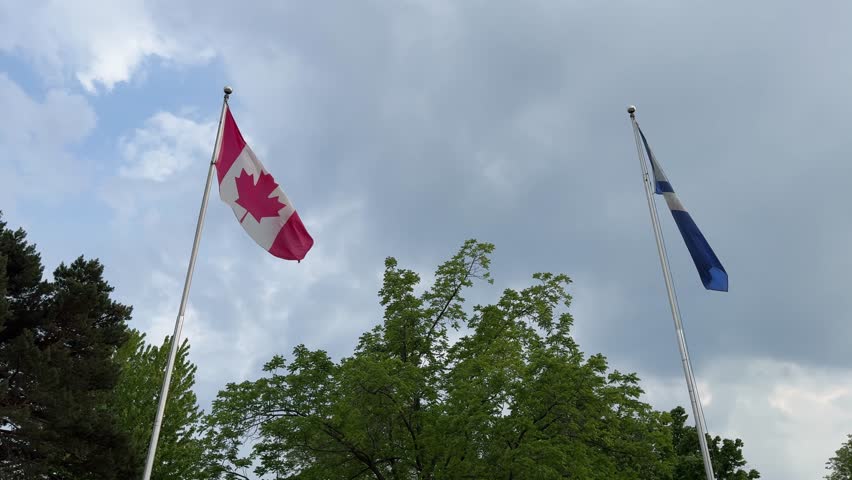 DOLLY SHOT - Canada flag and Toronto City flag waving atop a pole at Centreville Amusement Park on Centre Island, a small island in Lake Ontario, south of mainland Toronto, Ontario, Canada.