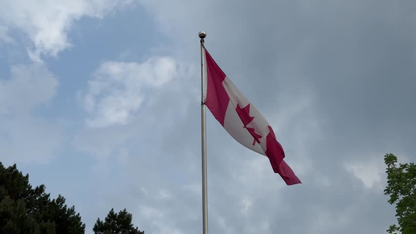 SLOW MOTION SHOT - The Canadian flag prominently flies atop a pole at Centreville Amusement Park on Centre Island, a small island in Lake Ontario, south of mainland Toronto, Ontario, Canada.