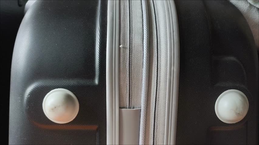 Closeup top view of silver zipper of hard shelled suitcase, new and clean luggage in black color made of Polycarbonate material. Female hands open the zipper of the suitcase.