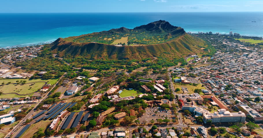 The Diamond Head Crater surrounded by the cityscape and waterscape of the Pacific Ocean. Drone footage over Honolulu, Hawaii, USA on sunny day.