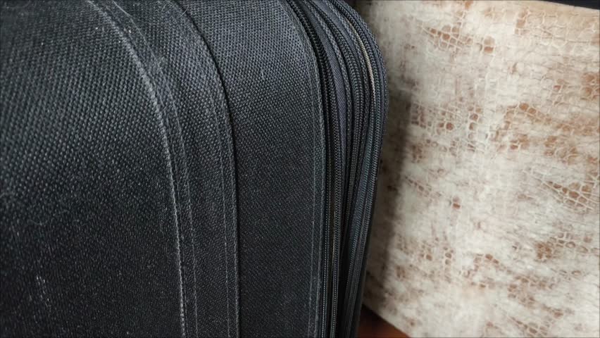 Closeup top view of silver zipper of hard shelled suitcase, new and clean luggage in black color made of Polycarbonate material. Female hands close the zipper of the suitcase.