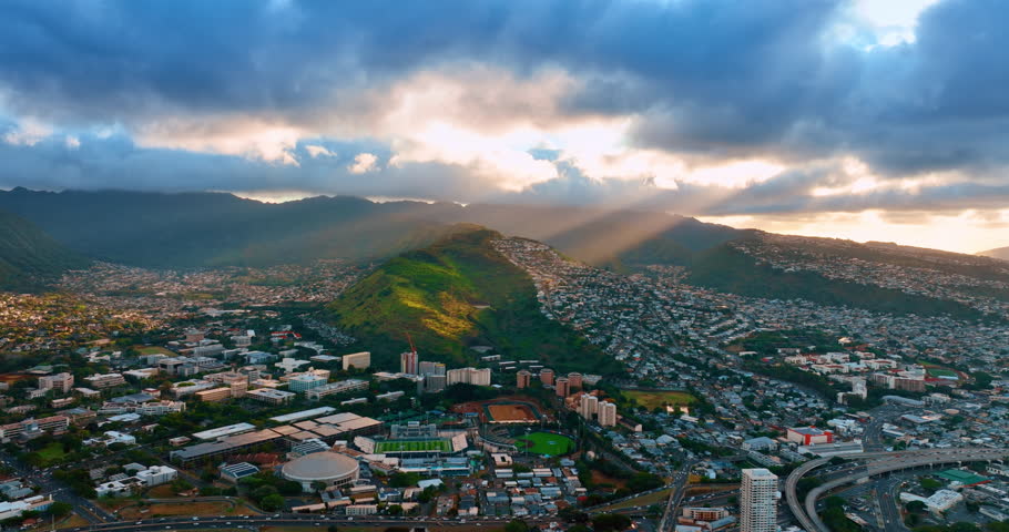 Beams of setting sun go through the huge cloudscape covering the sky over Honolulu, Hawaii, USA. Verdant mountain is lit with light ray. Aerial view.