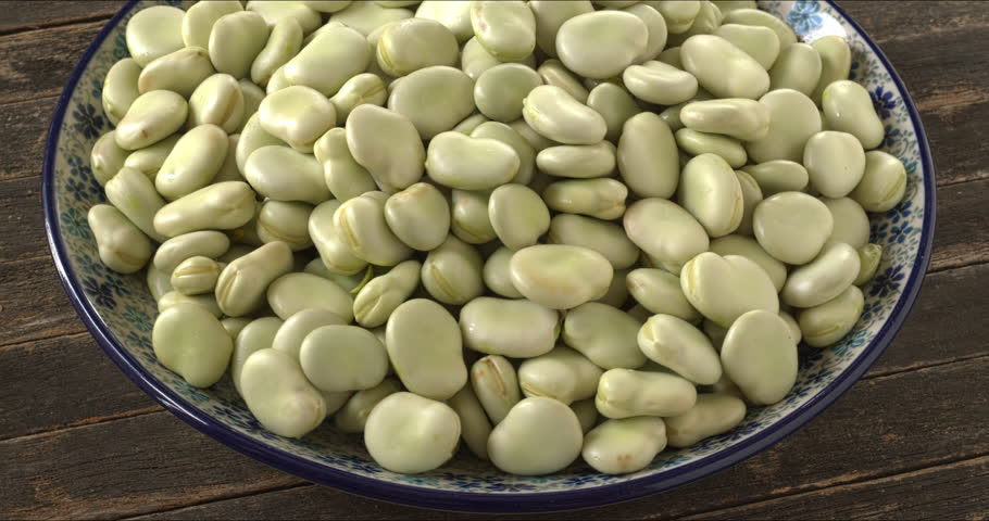 Raw fava beans (Vicia faba) with the second skin on a platter. Selective focus, table spin.