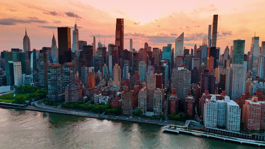 Approaching the waterfront of the East River in New York, USA. Aerial perspective on Manhattan at the backdrop of pink sky at sunset time.