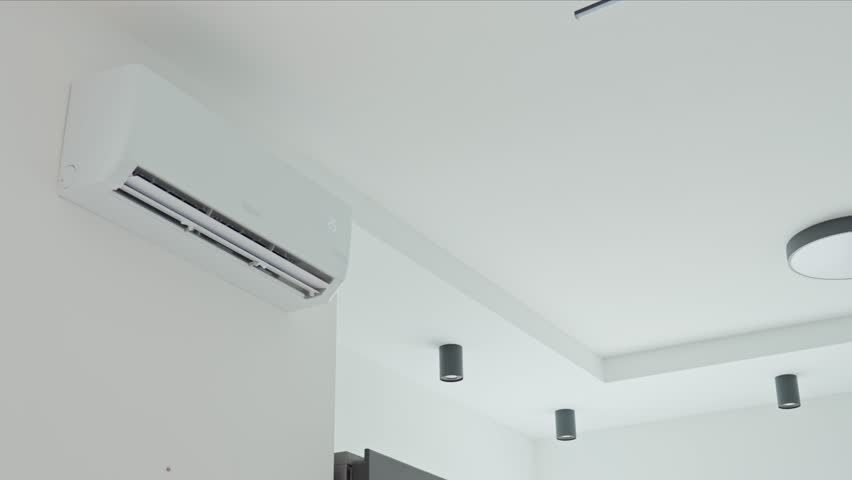 Close-up of hand using remote control to adjust temperature on wall-mounted air conditioner. Concept of indoor climate control and cooling during hot weather