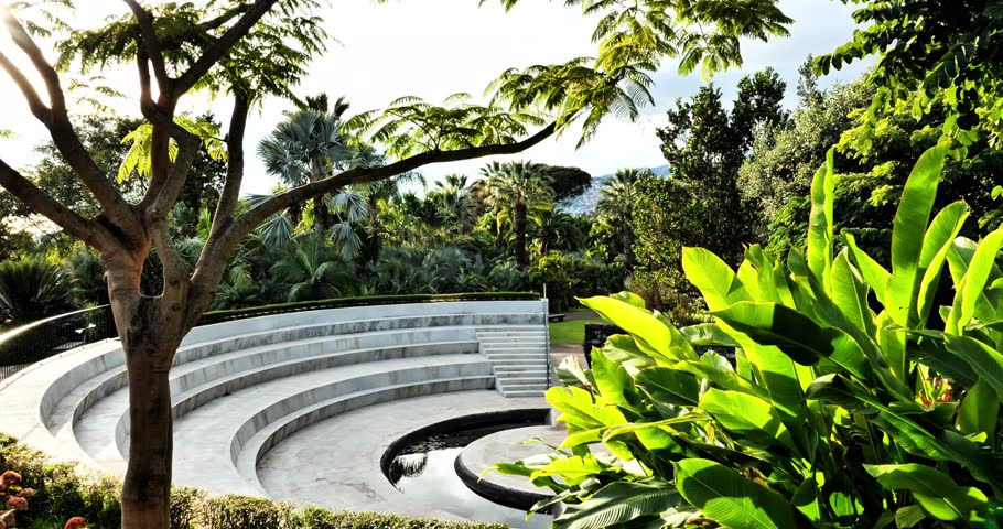 Modern amphitheater surrounded by lush tropical vegetation in a botanical garden on Madeira. Sunlight filters through green leaves, creating a peaceful and exotic atmosphere.