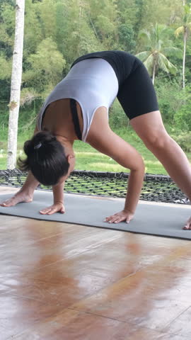 Vertical video. Woman finds peace in yoga practice on bamboo terrace overlooking tropical plants and rice paddies, slow motion 