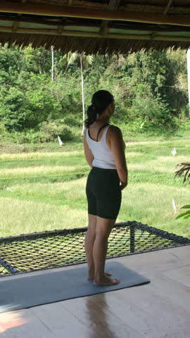 Vertical video. Yoga session on bamboo terrace in lush greenery and rice fields during peaceful tropical morning 