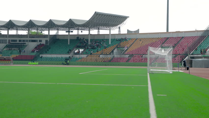 Shot from the corner of a football field, with the corner flag in the foreground, gently swaying in the wind. In the background, the pitch stretches out with crisp white lines, evoking the anticipatio