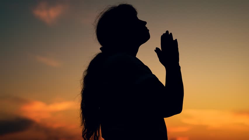 Faith in god. Christian woman praying at sunset close-up. Girl on background of sky in rays of sun prayer to family and children. Relaxation and meditation in nature. Apologize. Hope. Silhouette