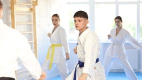 Diligent young woman attendee of karate classes practicing kata standing in row with others in sports hall. High quality 4k footage - Powered by Shutterstock - Get 15% off with code: PIKWIZARD15