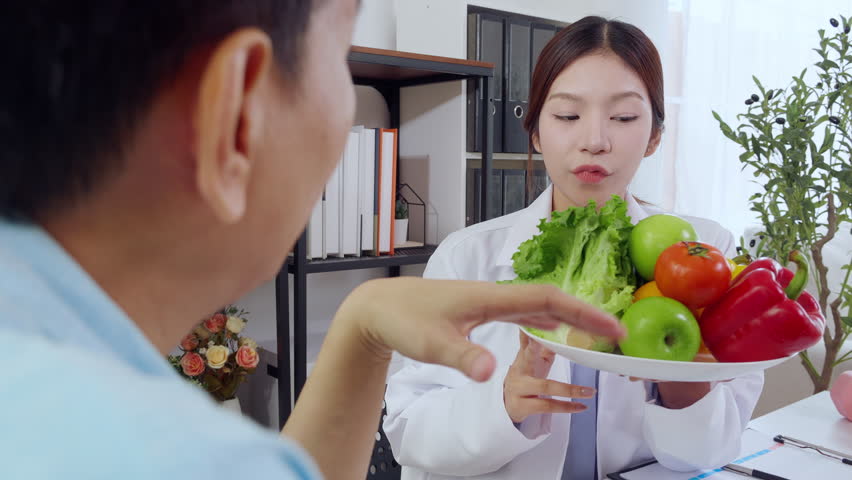 Asian nutritionist holding fresh fruits vegetables during consultation with patient in clinic, wellness and healthy eating, woman dietitian or consultation explaining nutrition for weight loss advice.
