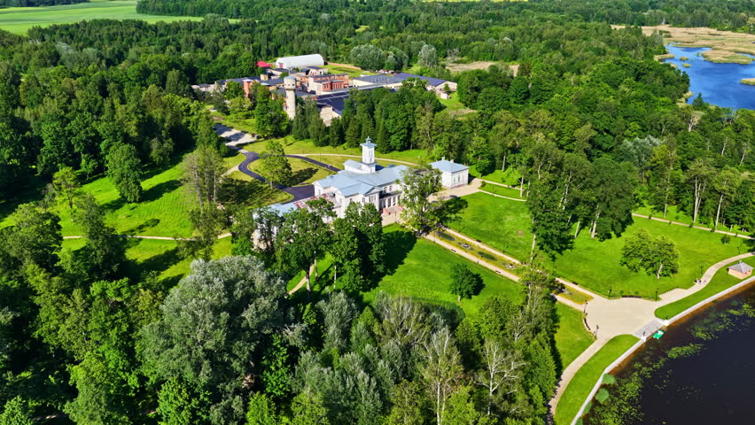 Aerial parallax movement reveals Astravas Manor, an Italian villa-style palace, nestled in lush parkland beside a scenic lake in Biržai, Lithuania.