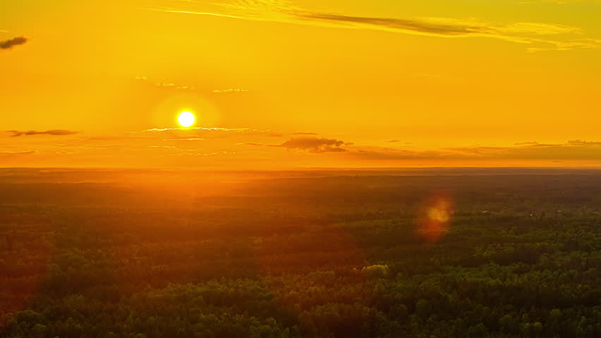 Time-lapse aerial view of a vivid sunset over a dense forest landscape in Latvia with glowing orange sky.