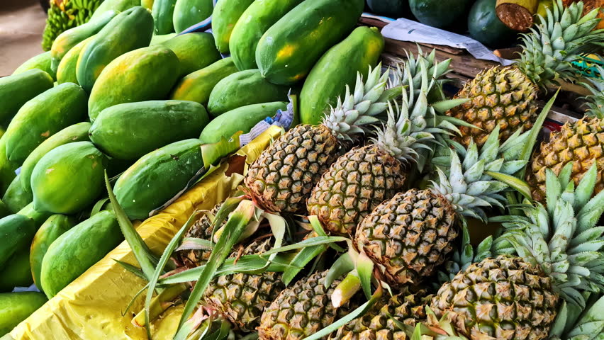 A colorful close-up shows an abundant pile of fresh green papayas and whole pineapples for sale at a rustic outdoor fruit stall, showcasing the local produce of Sri Lanka.