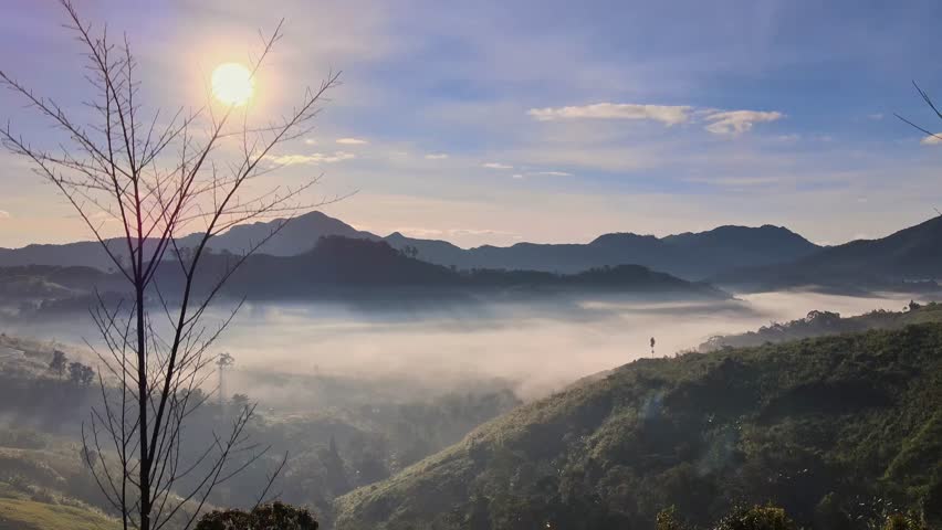 A breathtaking sunrise illuminates a serene mountain landscape, with dense mist filling the valleys below. The early morning light creates a peaceful and majestic natural scene.