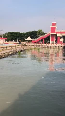 Surabaya, Indonesia - April 13, 2024, Kenjeran Beach promenade with red bridge and calm sea under clear sky, popular tourist spot in Surabaya, Indonesia.