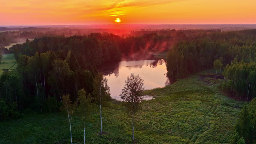 Golden sunset over forest lake with mist rising and trees reflecting in water